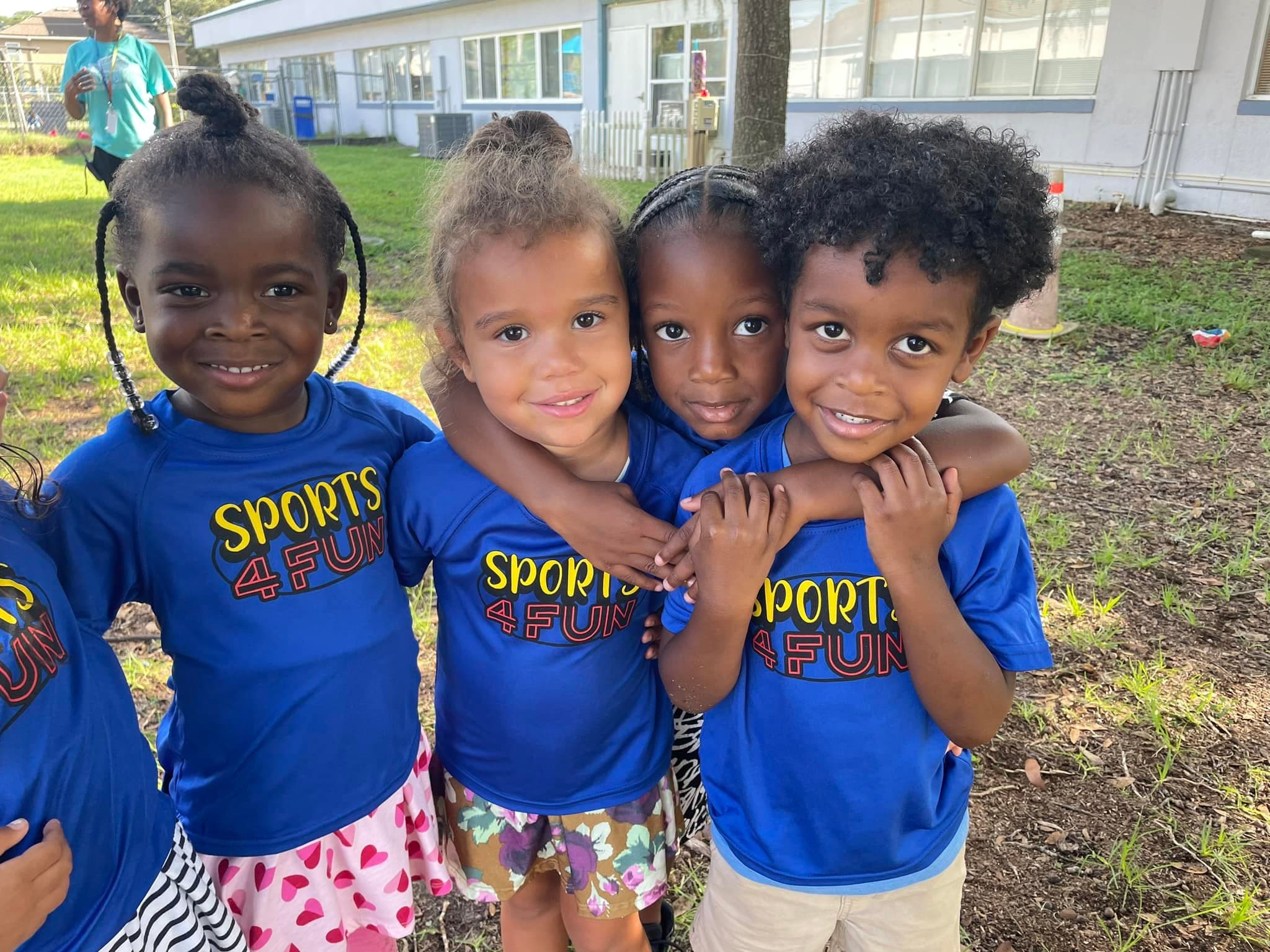 Four children in Sports4Fun shirts smiling together at a school program